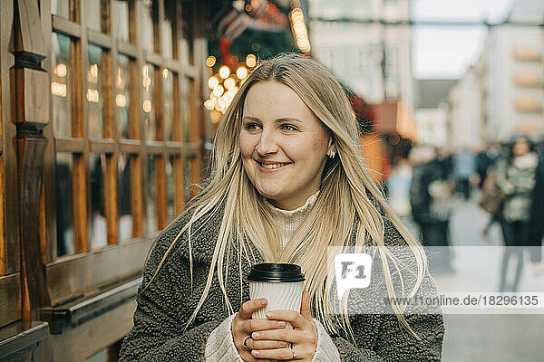 Happy blond woman with coffee cup standing on footpath at Christmas market