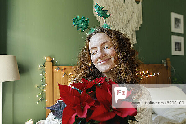 Smiling woman with eyes closed holding Poinsettia plant at home