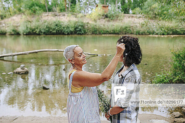 Senior woman decorating friend's hair with flower by lake in park