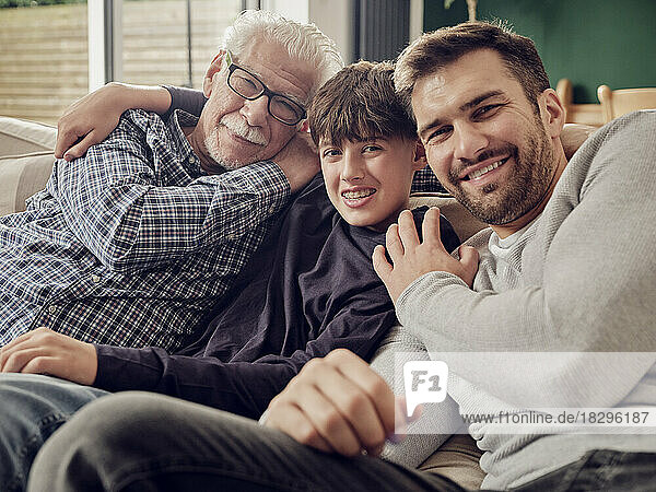 Happy grandfather  father and son sitting together on couch in living room