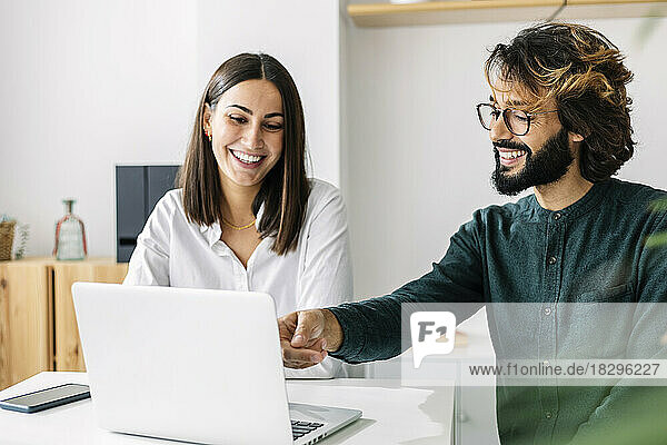 Happy businessman discussing with colleague over laptop at workplace
