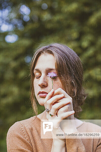 Frau berührt geschlossene Augen mit Blume