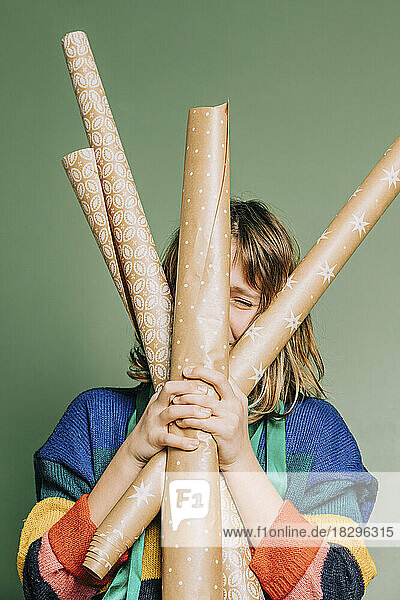 Girl with wrapping paper rolls standing in front of green wall
