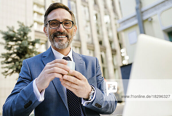 Happy mature businessman wearing eyeglasses holding coffee cup in cafe