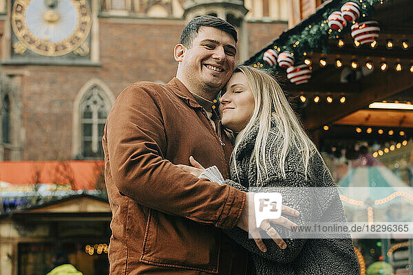Glücklicher Mann umarmt Frau auf dem Weihnachtsmarkt