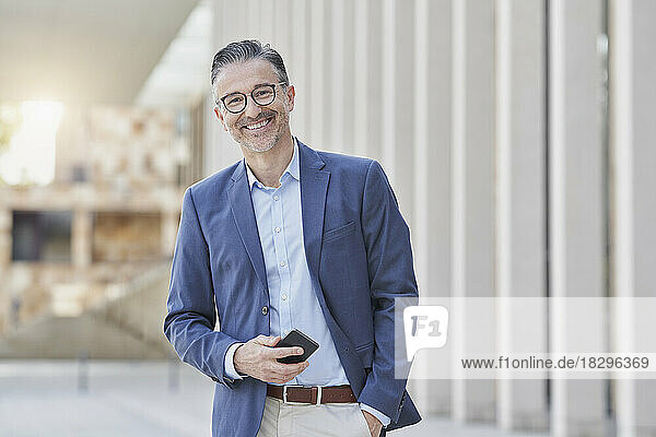 Happy mature businessman standing with mobile phone