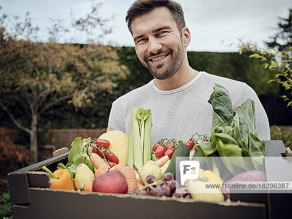 Smiling man carrying a fresh vegetable box in garden