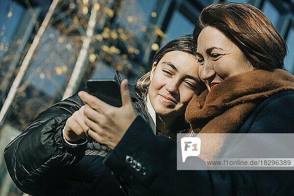 Smiling mother and daughter using smart phone on sunny day