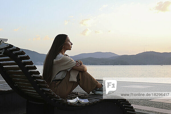 Thoughtful woman sitting on deck chair at sunset