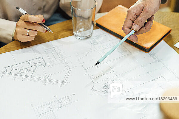 Hand of businessman pointing with pen on blueprint by colleague at table