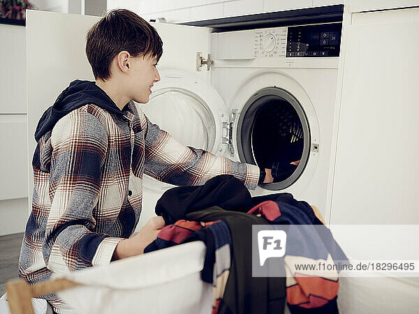 Boy putting laundry into washing machine at home