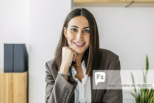 Glückliche junge Geschäftsfrau mit der Hand am Kinn im Büro