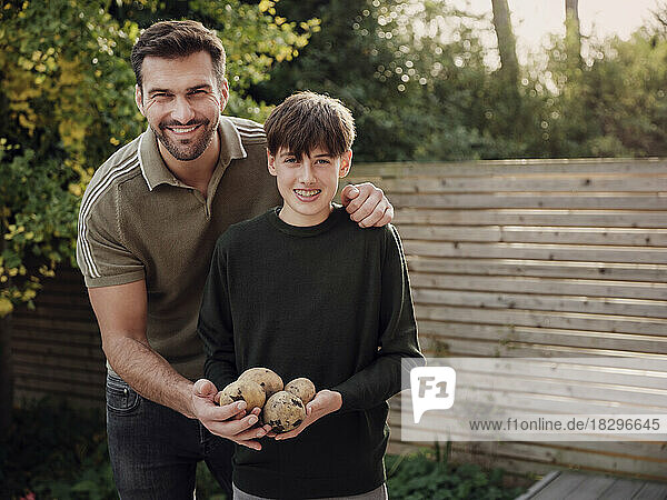 Vater und Sohn stehen im Garten und halten frisch geerntete Kartoffeln in der Hand