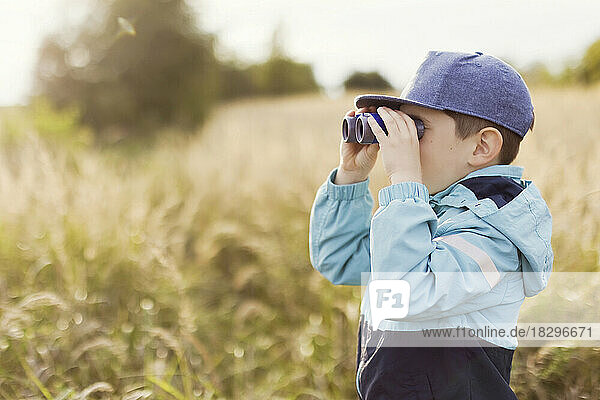Boy looking through binoculars on field