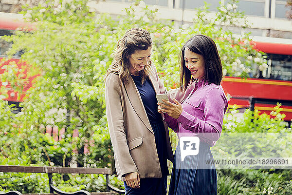 Happy businesswomen using mobile phone with colleague at park