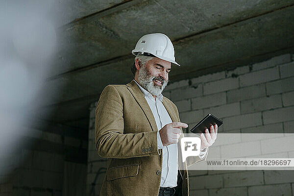 Happy architect using tablet PC standing at under construction site