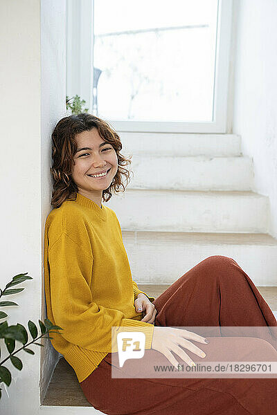 Smiling young woman sitting on staircase at home