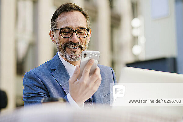 Happy mature businessman looking at smart phone at cafe