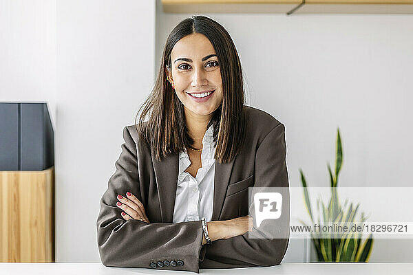 Smiling young businesswoman with arms crossed at workplace