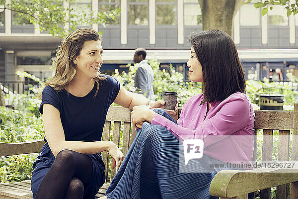 Smiling businesswoman holding coffee cup and talking with colleague in park