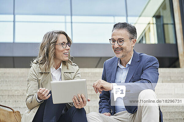 Lächelnde Geschäftsfrau hält Tablet-PC in der Hand und diskutiert mit Kollegen über Schritte