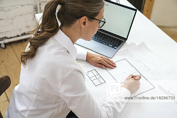 Businesswoman with blueprint on desk in office