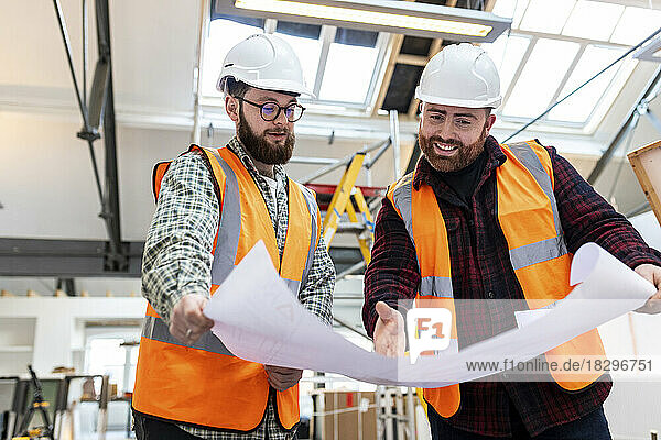 Happy engineer with colleague discussing over blueprint at construction site