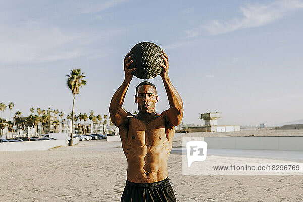 Active man holding ball and exercising on beach