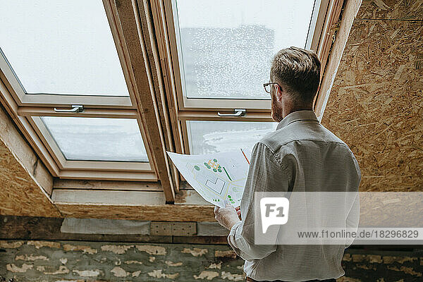 Architect standing with blueprint near window at construction site