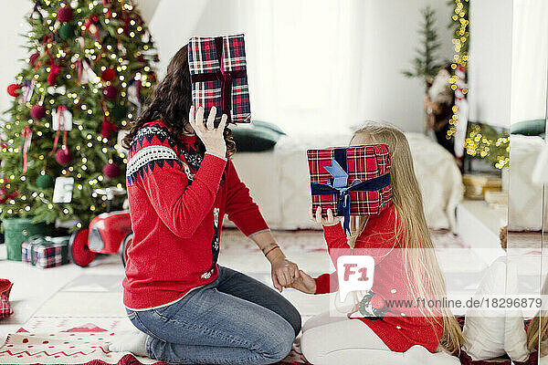 Mutter und Tochter bedecken zu Hause ihr Gesicht mit Geschenken