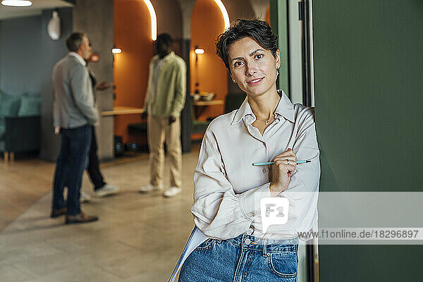 Smiling businesswoman leaning on wall in office
