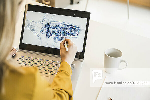 Woman drawing wind turbine part on laptop at desk