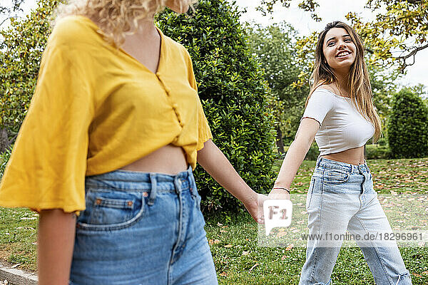 Smiling woman holding friend's hand walking in park