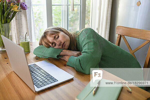 Tired freelancer sleeping on table in kitchen at home