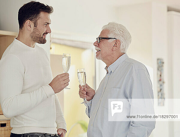 Senior man and adult son tcelebrating at home toasting with champagne