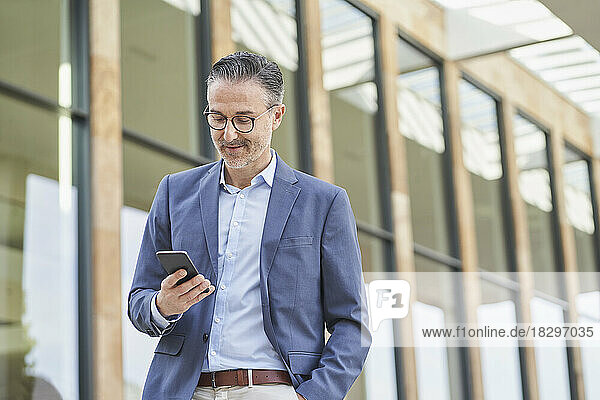 Smiling businessman using mobile phone outside building