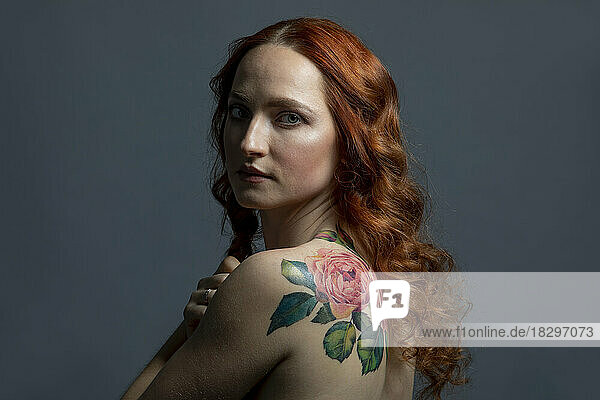 Beautiful woman with flower tattoo against gray background