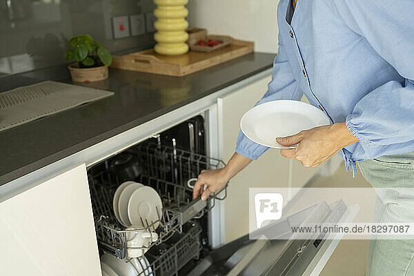 Hands of woman loading plates in dishwasher at home