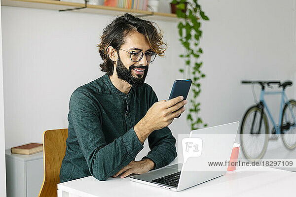 Happy bearded businessman using smart phone at desk in office