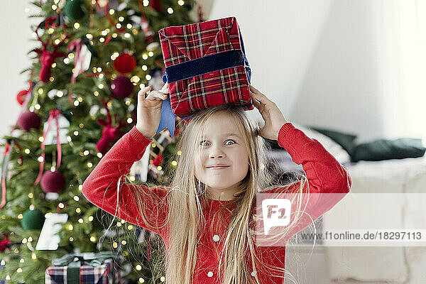 Surprised girl holding Christmas gift on head at home