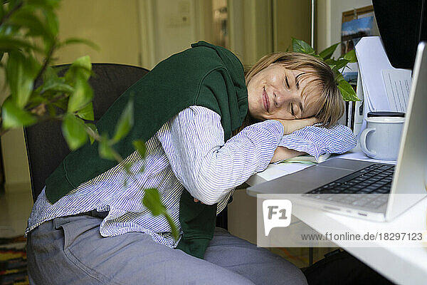 Smiling freelancer sleeping on table at home