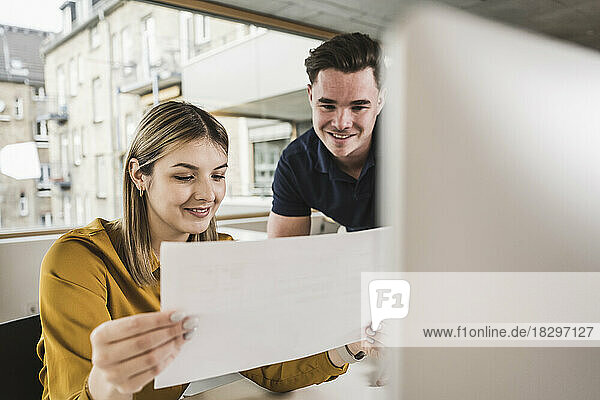 Smiling young businesswoman reading document with colleague in office