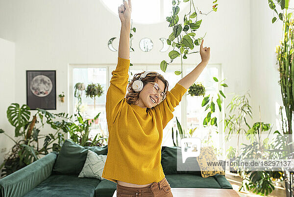 Happy young woman wearing headphones dancing at home