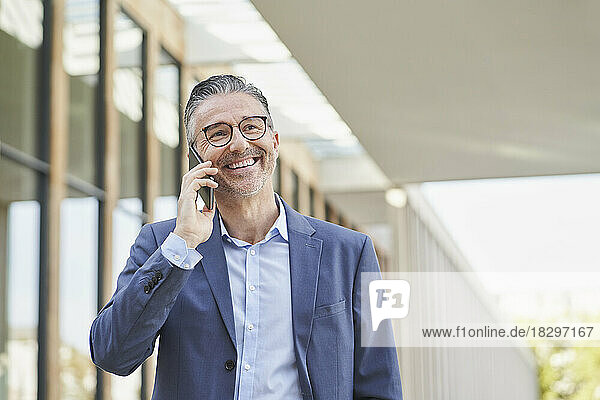 Happy mature businessman talking on mobile phone outside building