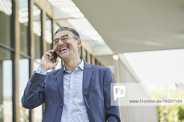 Happy businessman talking on smart phone outside building