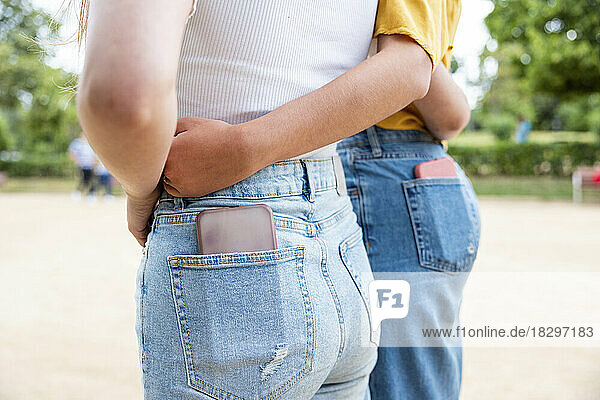 Lesbian couple with smart phone in pockets embracing each other in park