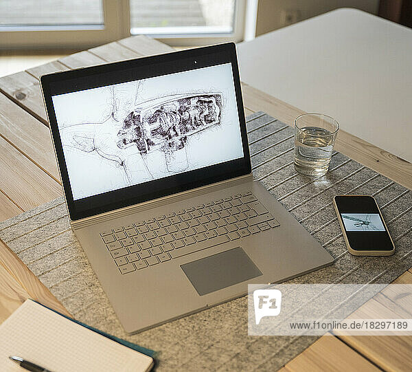 Drawing of wind turbine on laptop screen kept by smart phone at desk