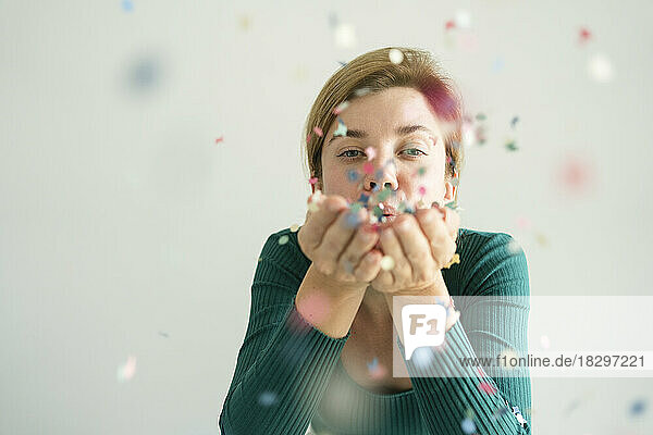 Woman blowing confetti in front of white wall