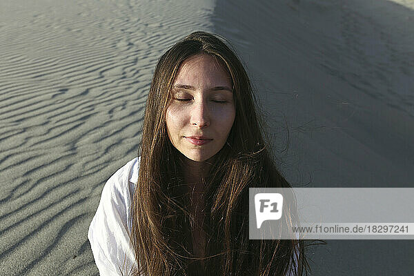 Junge Frau mit geschlossenen Augen sitzt am Strand