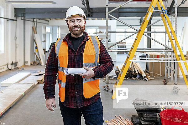 Happy engineer standing with rolled document at construction site